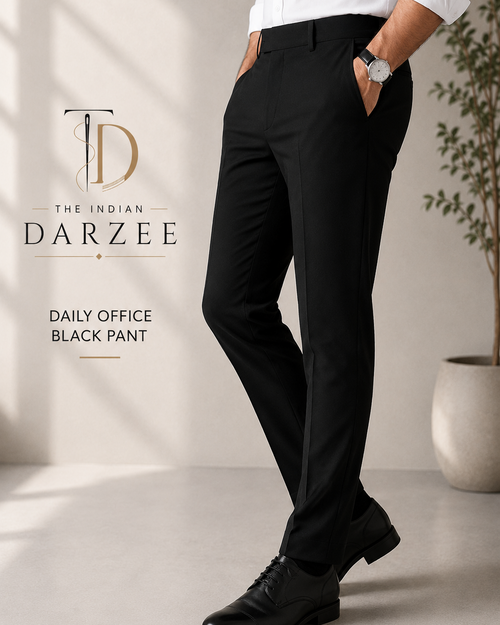A man wearing black Darzee daily office pants, a white dress shirt, and black dress shoes, standing in a bright indoor setting with a plant in the background. The brand logo 'The Indian Darzee' is visible on the left.
